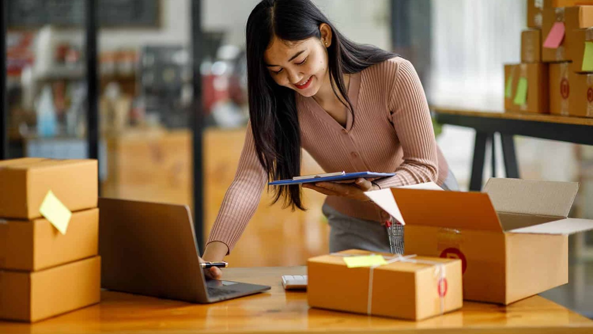 a lady using a laptop while holding a phone and some boxes on the table